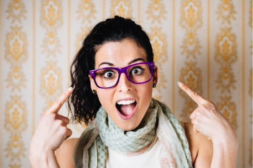Woman wearing purple glasses, pointing at them with both hands and making an excited expression.