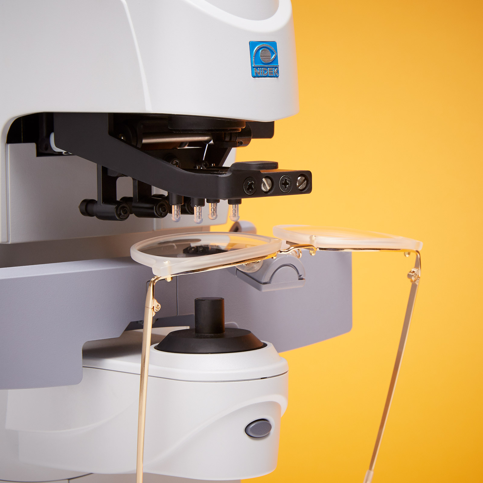 Optical lens edger with glasses in place, NIDEK branding visible.