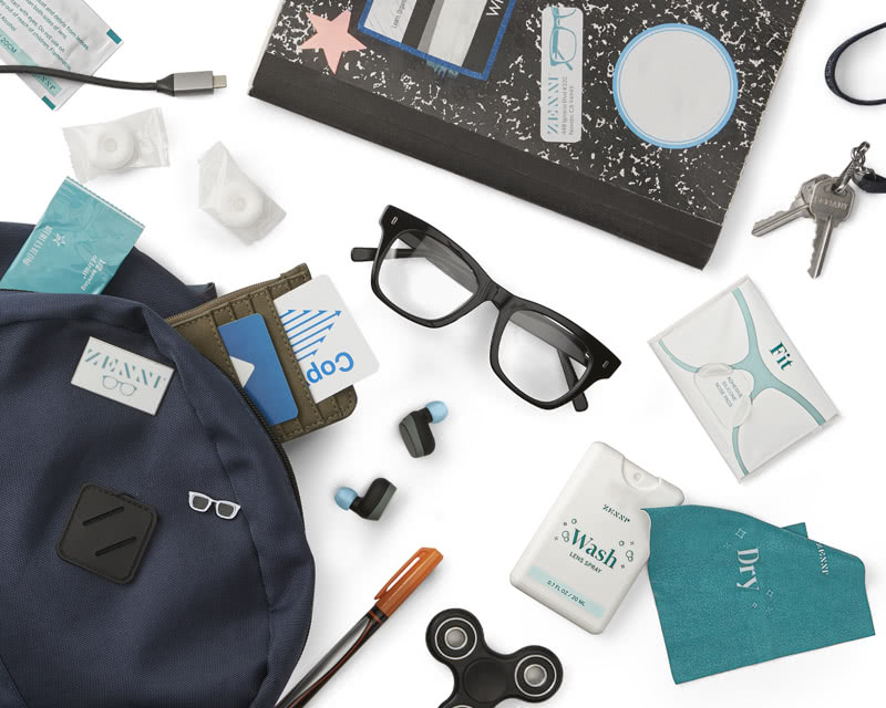Black square-framed glasses surrounded by a wallet, a notebook, earplugs, a pen, and cleaning supplies.