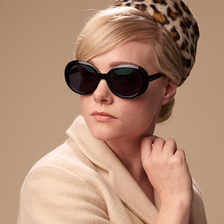Woman wearing oversized black sunglasses and a beige coat, styled with a leopard-print headscarf.