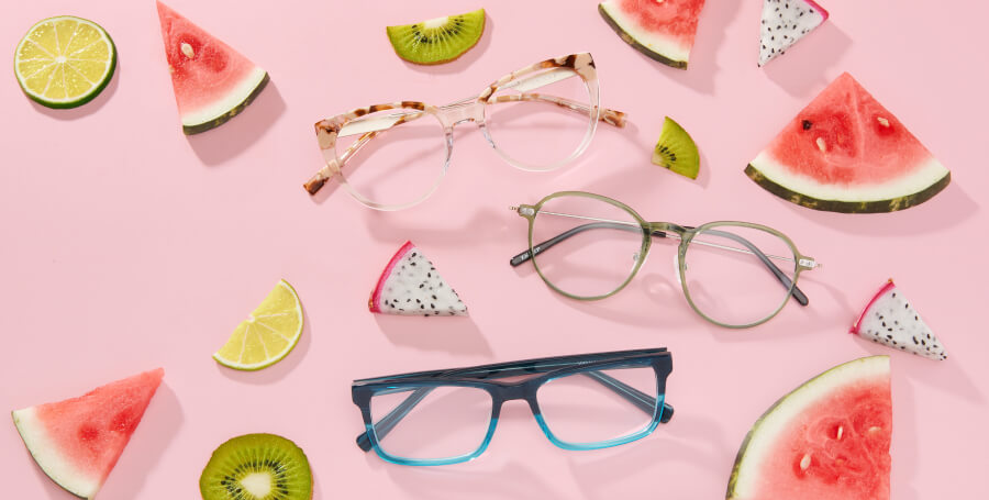 Three pairs of eyeglasses with various frame styles and colors placed among slices of fruit.