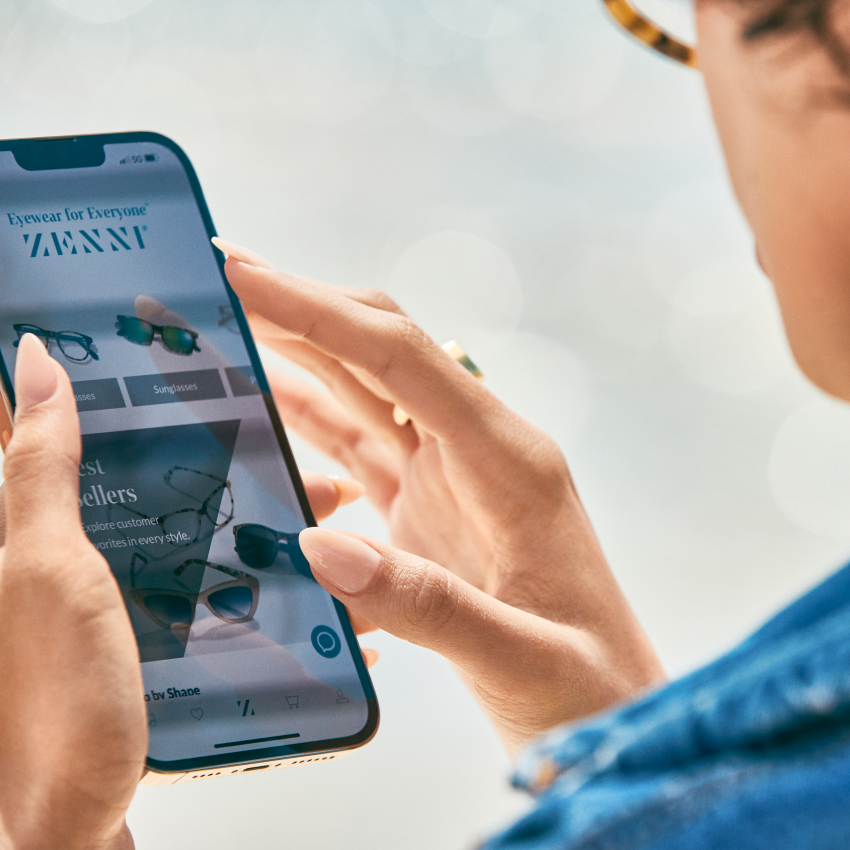 Person browsing "ZENNI - Eyewear for Everyone" on a smartphone, showing images of sunglasses.