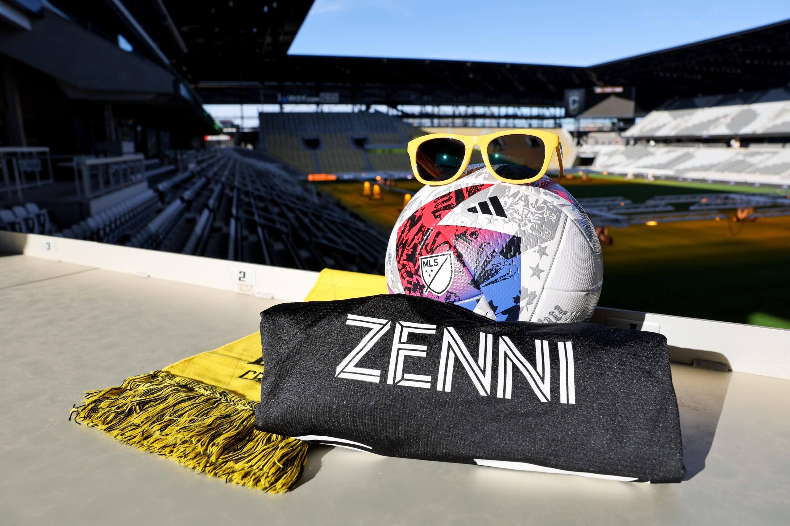 Soccer ball with MLS logo, yellow sunglasses, black bag with "ZENNI," and yellow tassel-edged item.