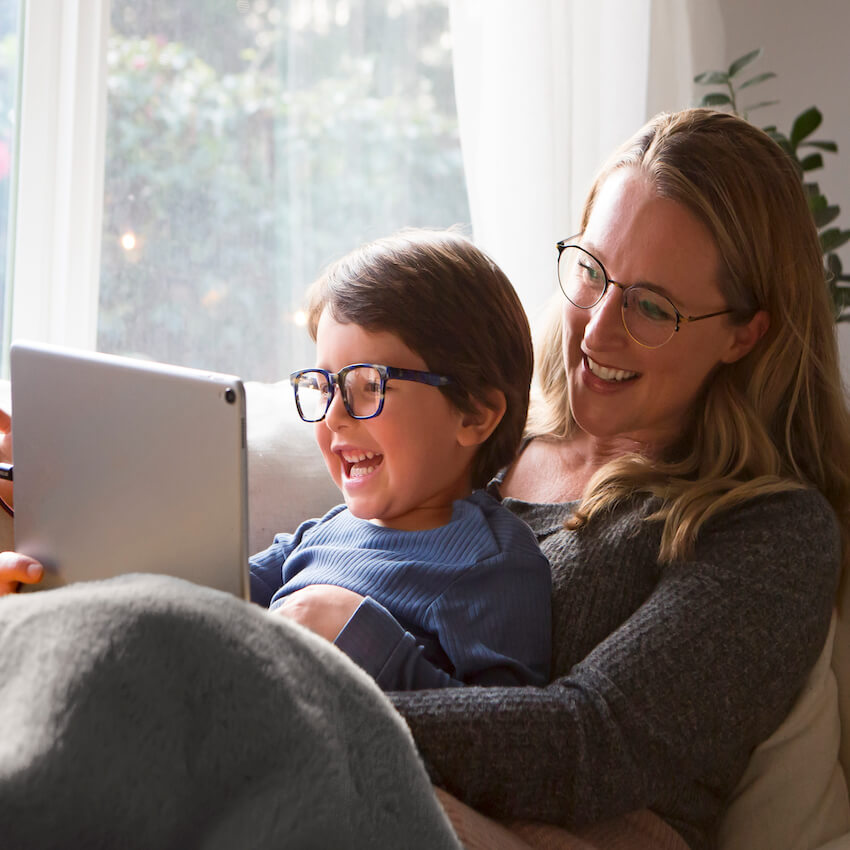 Child and adult wearing glasses, smiling while using a tablet.