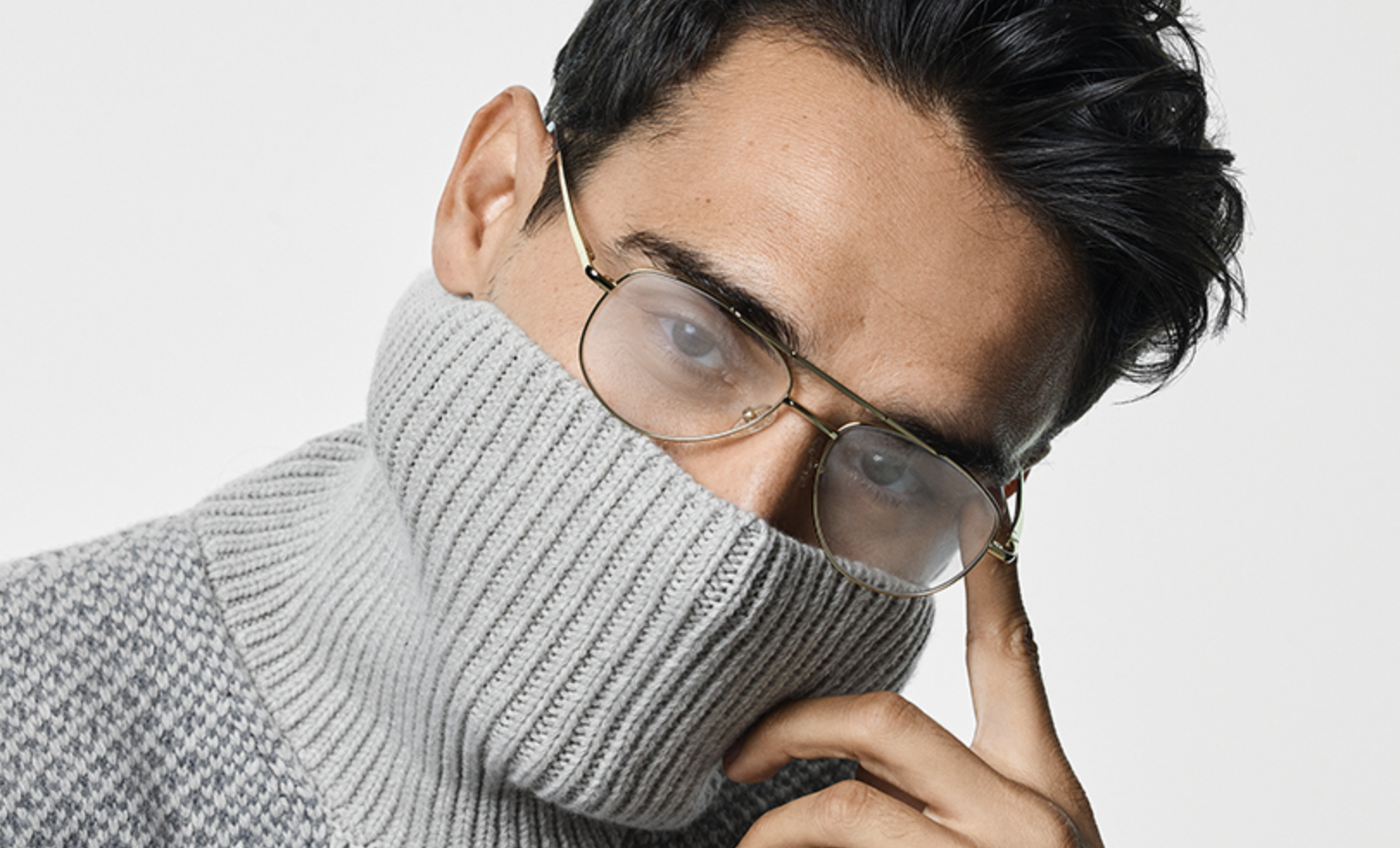 Man wearing gray turtleneck sweater and round glasses, partially covering face with the sweater's collar.