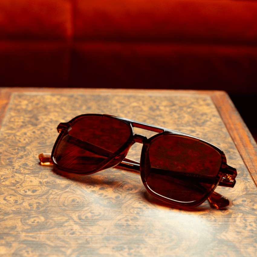 Brown aviator-style sunglasses with dark lenses, resting on a patterned surface.