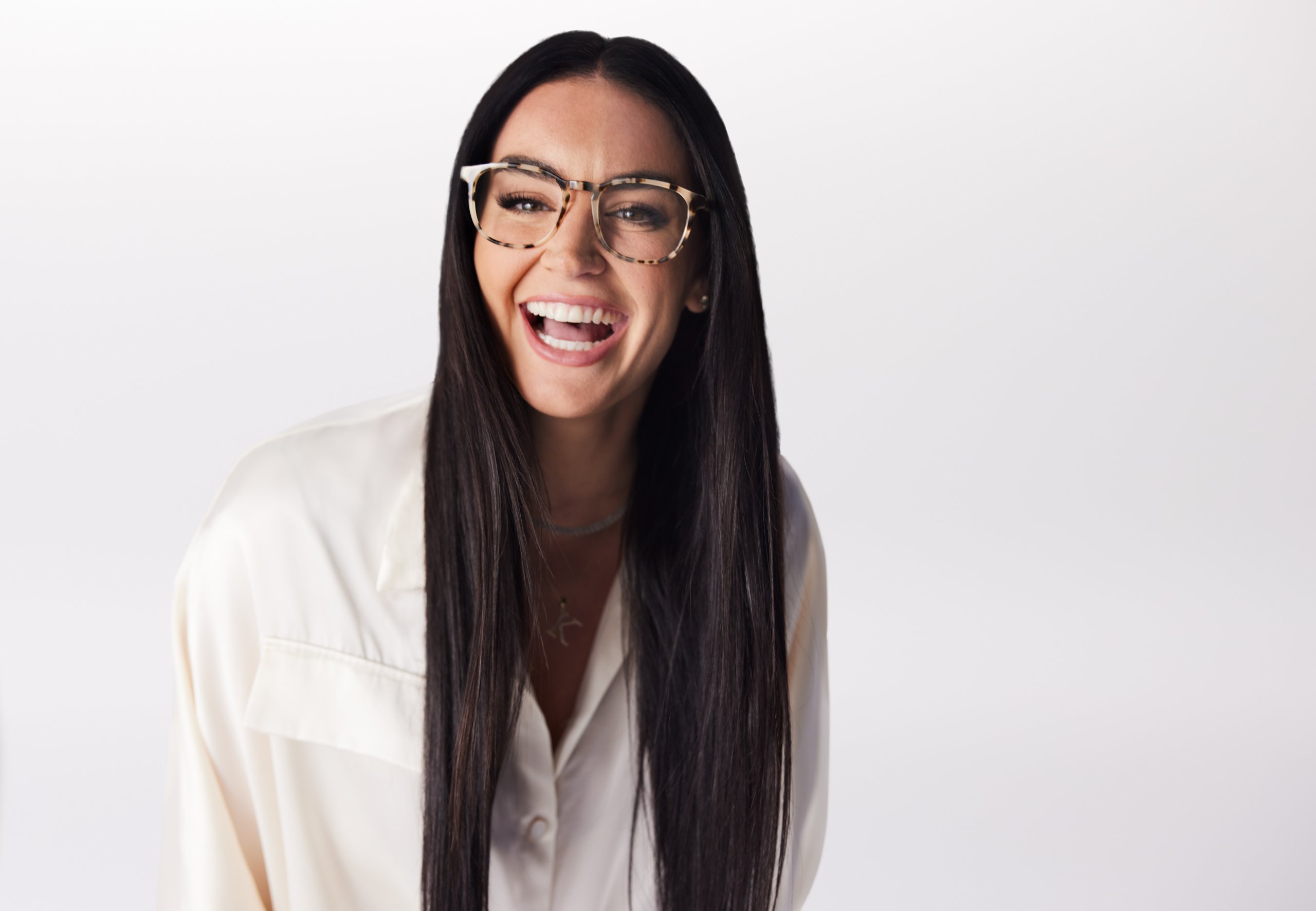 Woman wearing patterned glasses and a white button-up shirt, smiling widely.