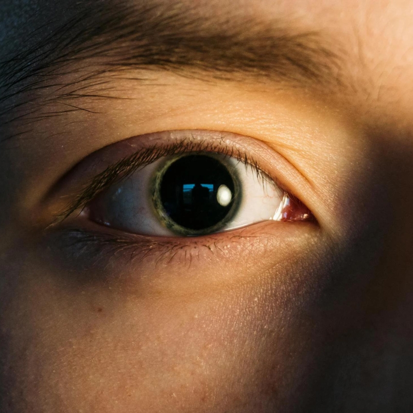 Close-up of a person's eye with a large pupil, showing details of the iris and eyelashes.