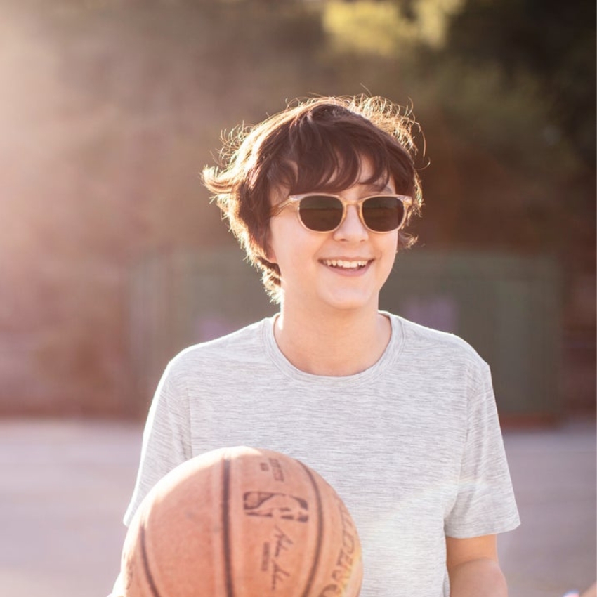 Person wearing sunglasses, holding a basketball with the NBA logo and signatures, smiling outdoors.