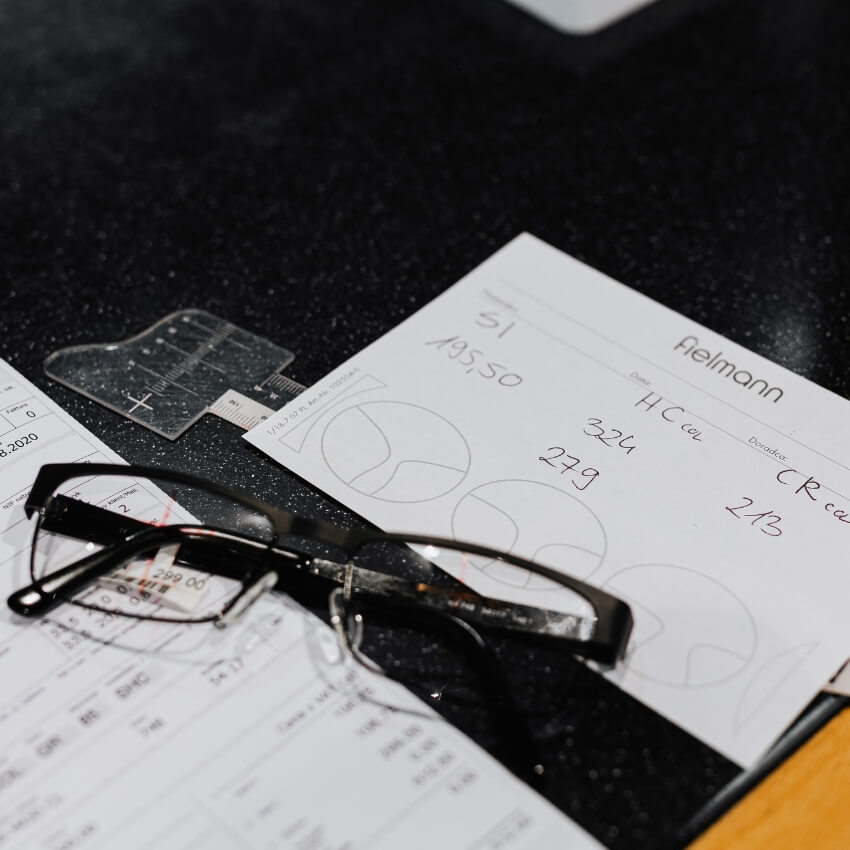 Glasses placed on paper with handwritten notes and diagrams. Text includes: "51 AB550, Aelmann, 324, 279, HC cal, CR cal 2/13".