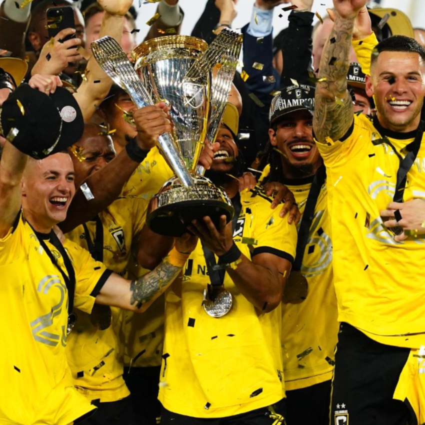Soccer team in yellow jerseys celebrating with a silver trophy adorned with gold accents.