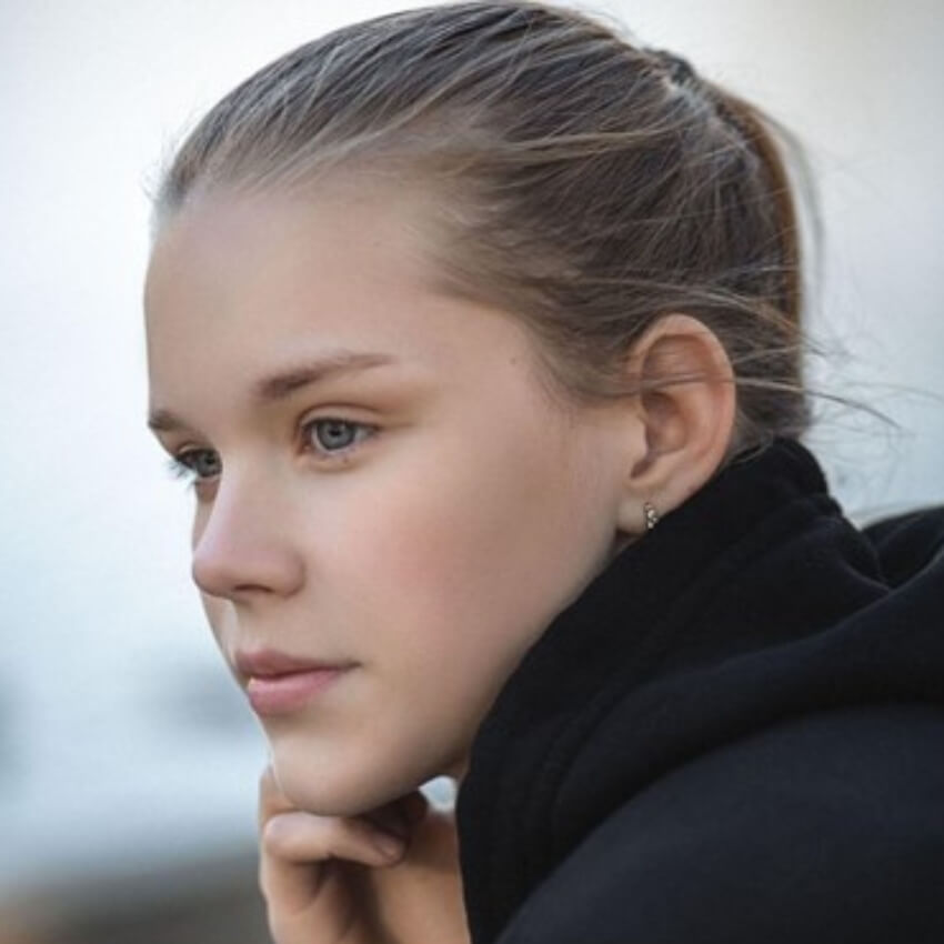 Person with blonde hair tied back, wearing a black top, looking to the side with a contemplative expression.