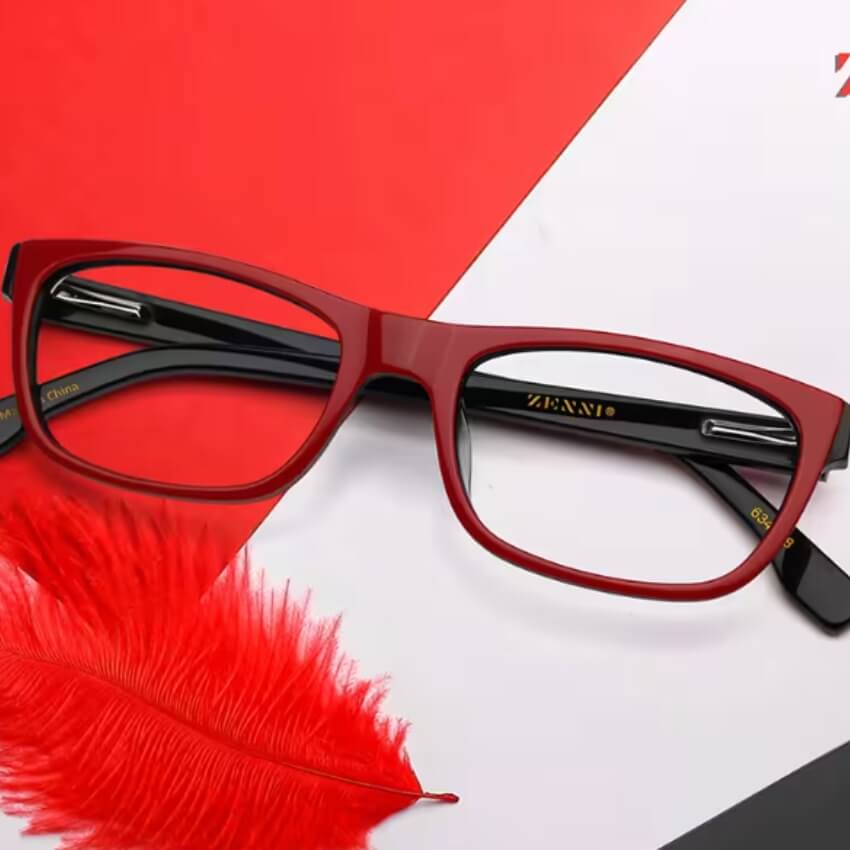 Red rectangular eyeglasses with black arms inscribed "ZENNI" and "China," laying on a multicolored surface.