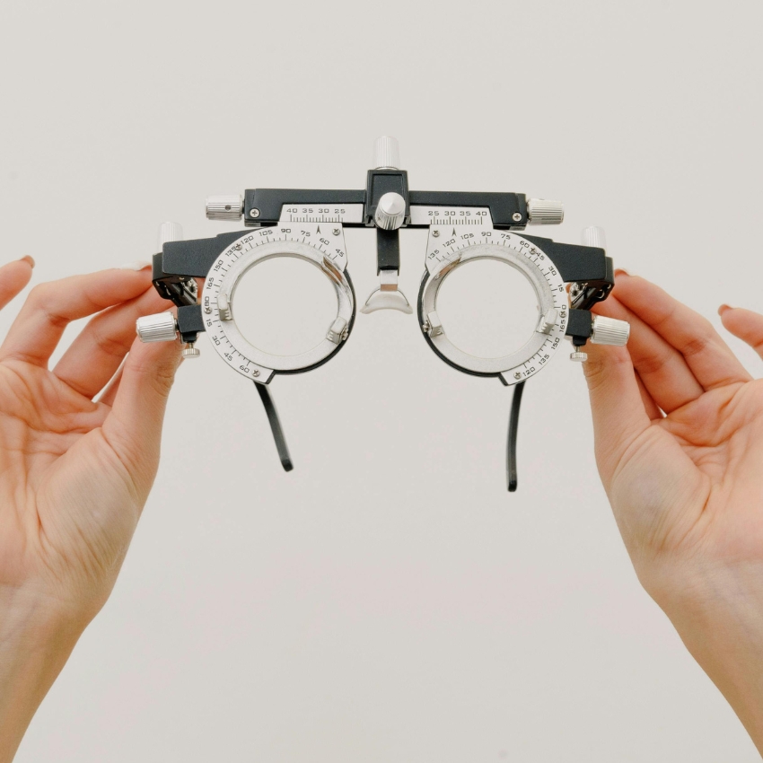 Hands holding a trial lens frame used by optometrists for vision testing, featuring adjustable dials.
