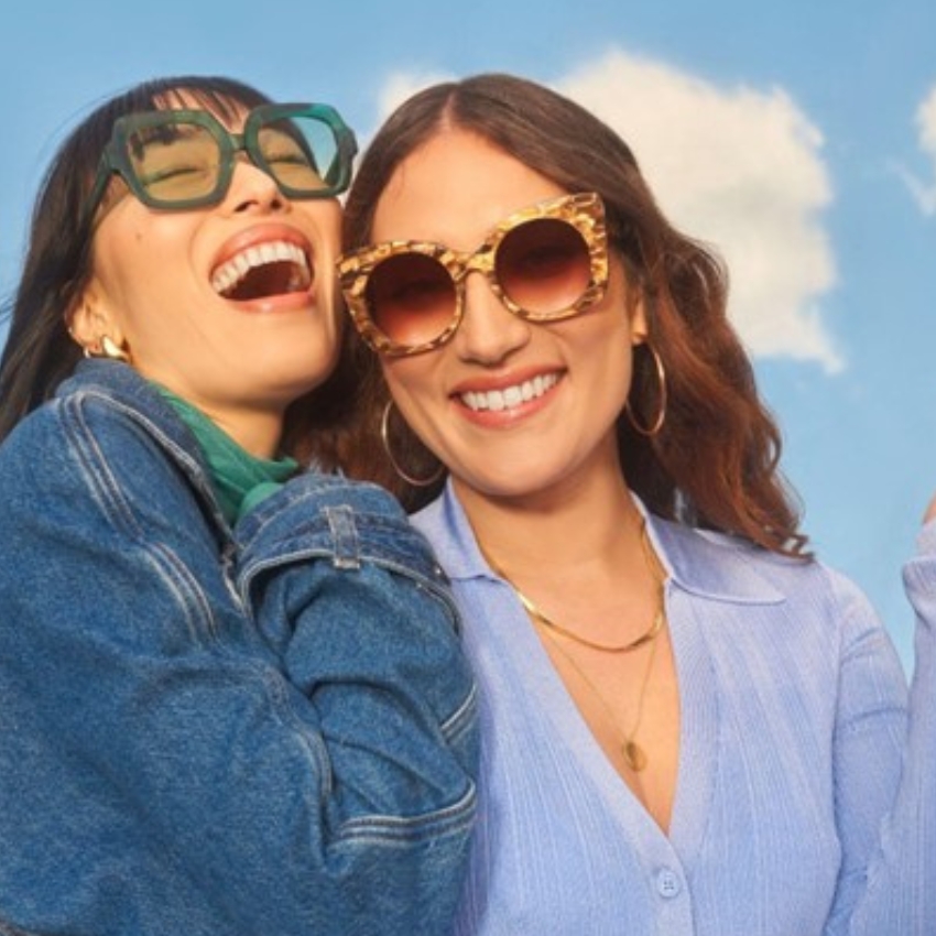 Two women wearing stylish sunglasses, one with green square frames and the other with round tortoiseshell frames.