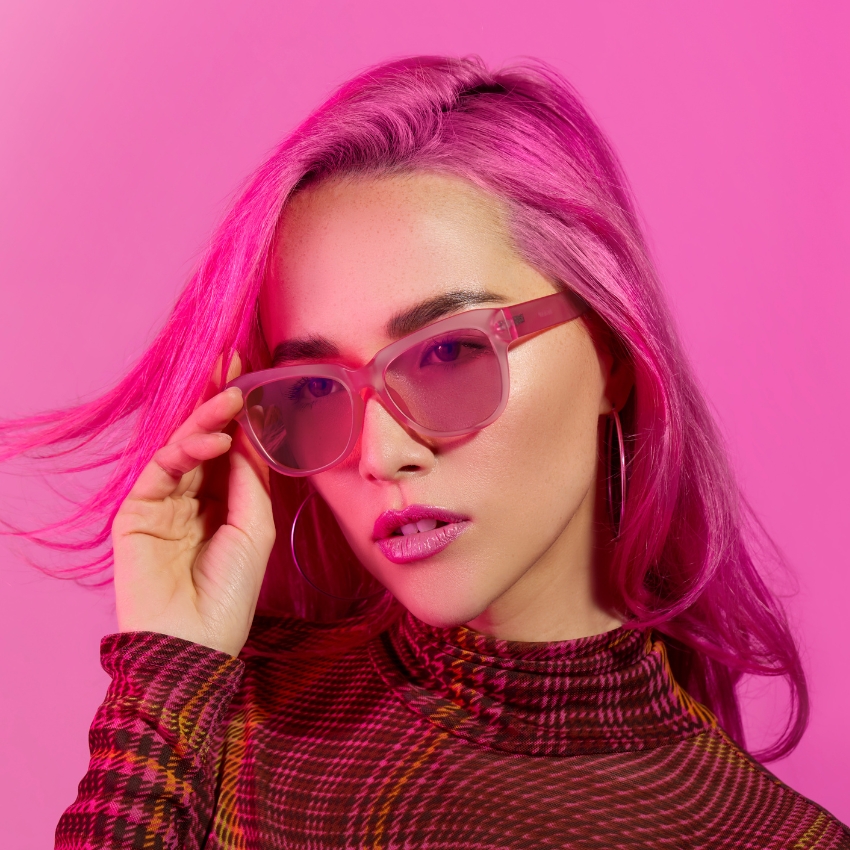 Woman wearing pink-tinted sunglasses with pink hair and checkered turtleneck.