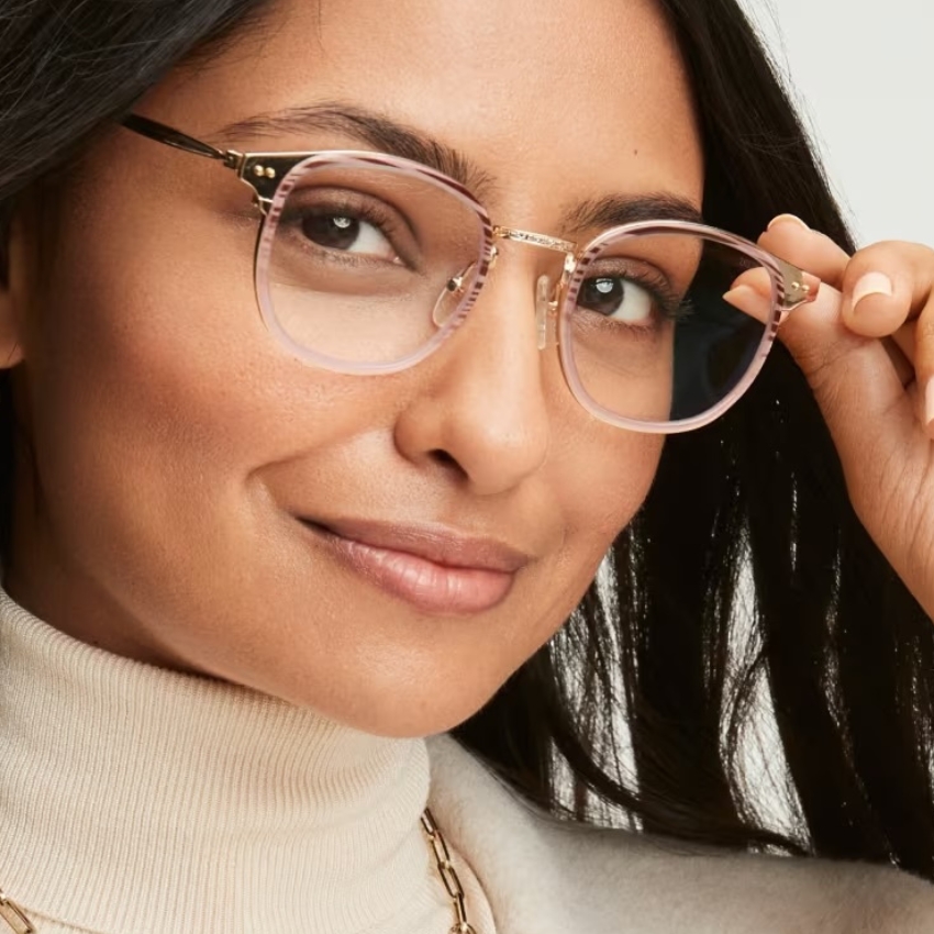 Woman wearing round, thin-framed eyeglasses with a light pink tint and gold accents.