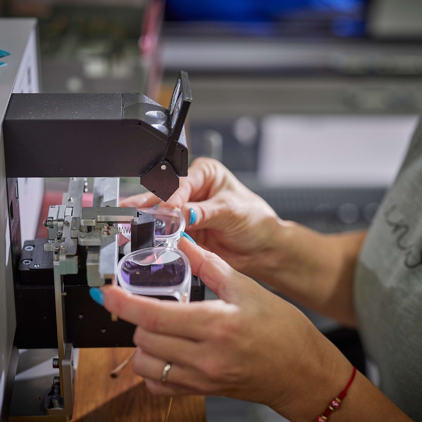 Hands adjusting eyeglasses under a lens-making machine.