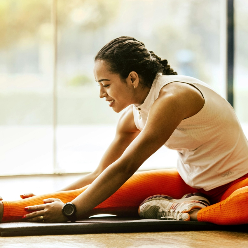 Woman wearing a white sleeveless top and orange leggings stretching on a yoga mat.