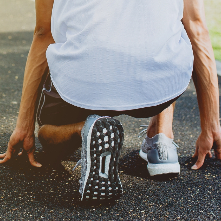 Gray running shoes with textured sole, shown from behind as a person crouches in a starting position.
