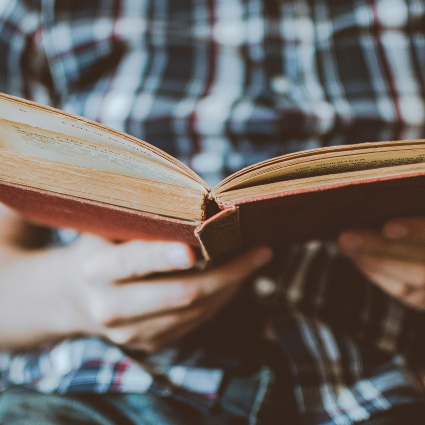 Hands holding an open vintage book with weathered pages and a red cover.