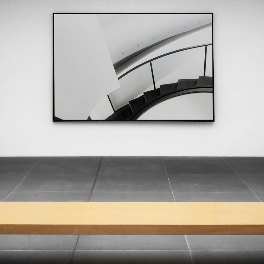 Framed abstract image of a spiral staircase with black railing on a white wall.