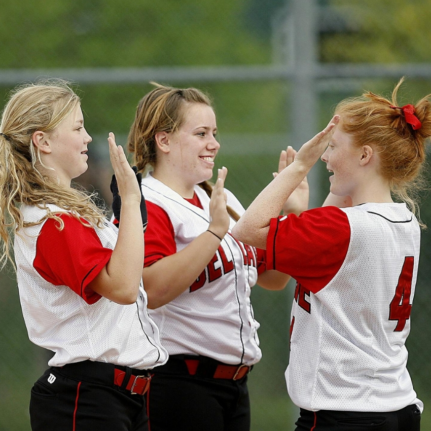 Softball players in red and white jerseys from team number 4 celebrate with high-fives.